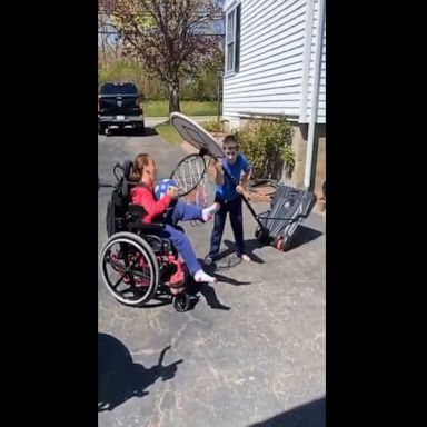 Brother helps his sister by lowering the basketball net down to her wheelchair.