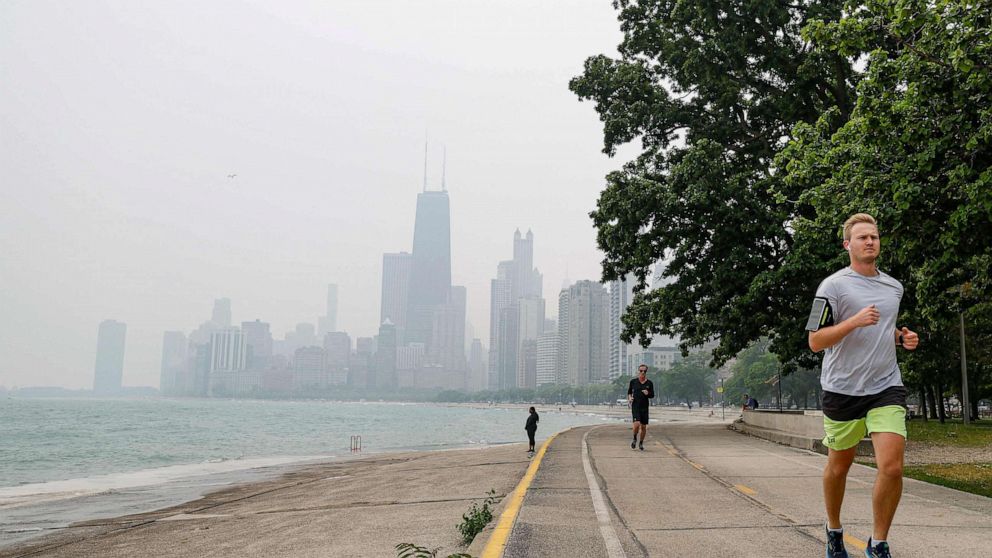 PHOTO: Joggers run along the shoreline of Lake Michigan with heavy smoke from the Canadian wildfires in the background, on June 27, 2023, in Chicago.