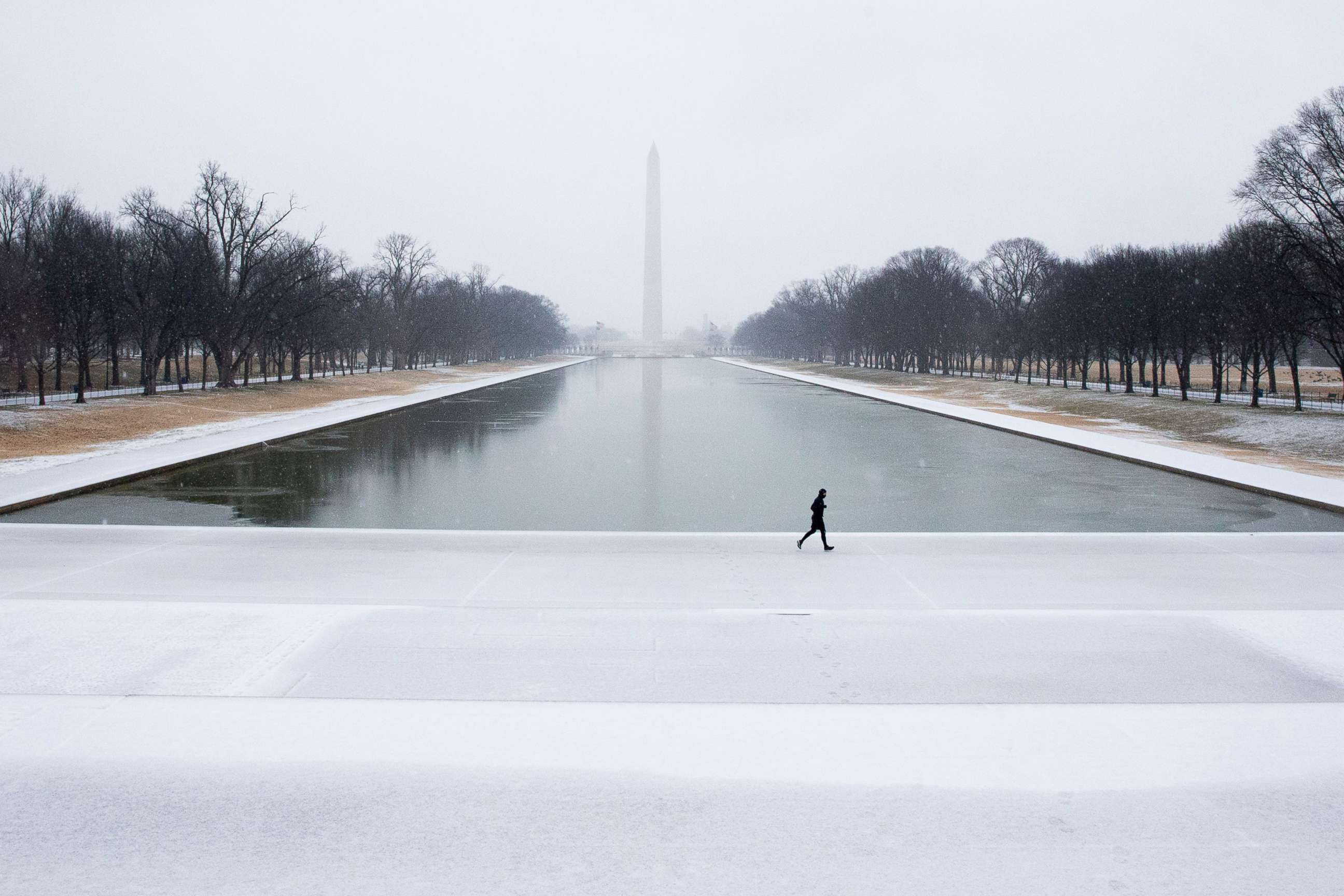 PHOTO: A runner jogs over a mixture of snow and freezing rain accumulating on the ground at the Lincoln Memorial Reflecting Pool, with the Washington Monument seen behind, in Washington, D.C., Feb. 18, 2021.