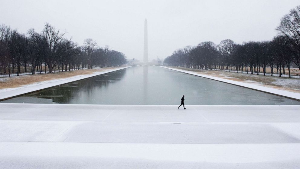 PHOTO: A runner jogs over a mixture of snow and freezing rain accumulating on the ground at the Lincoln Memorial Reflecting Pool, with the Washington Monument seen behind, in Washington, D.C., Feb. 18, 2021.