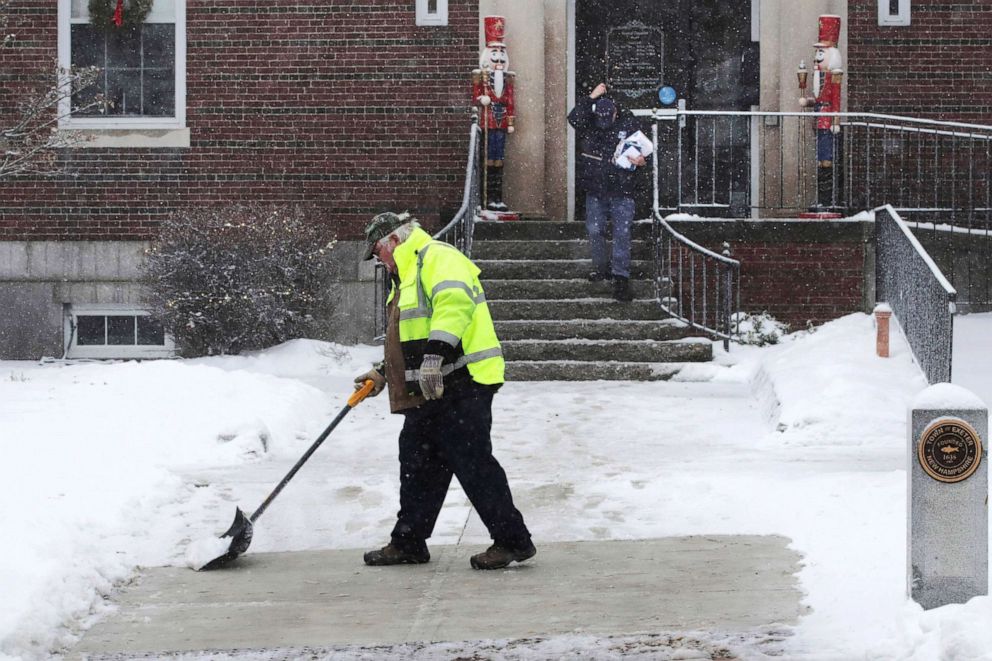 PHOTO: A worker shovels a coating of crusty snow from the walkway outside town hall during a snow storm in Exeter, N.H., Dec. 30, 2019. The southern New Hampshire area received a coating of snow and ice during the winter storm.