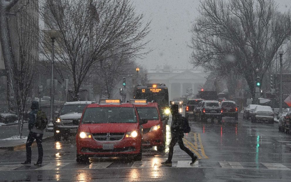 PHOTO: Pedestrians cross 16th Street near the White House (background) during the latest storm to hit the U.S. east coast, March 21, 2018, in Washington, DC.