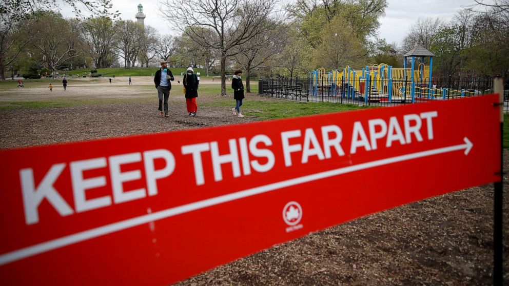 PHOTO: A sign by the New York City Department of Parks and Recreation indicates the appropriate measurement for social distancing as pedestrians linger in a field at Fort Greene Park in New York on April 14, 2020.