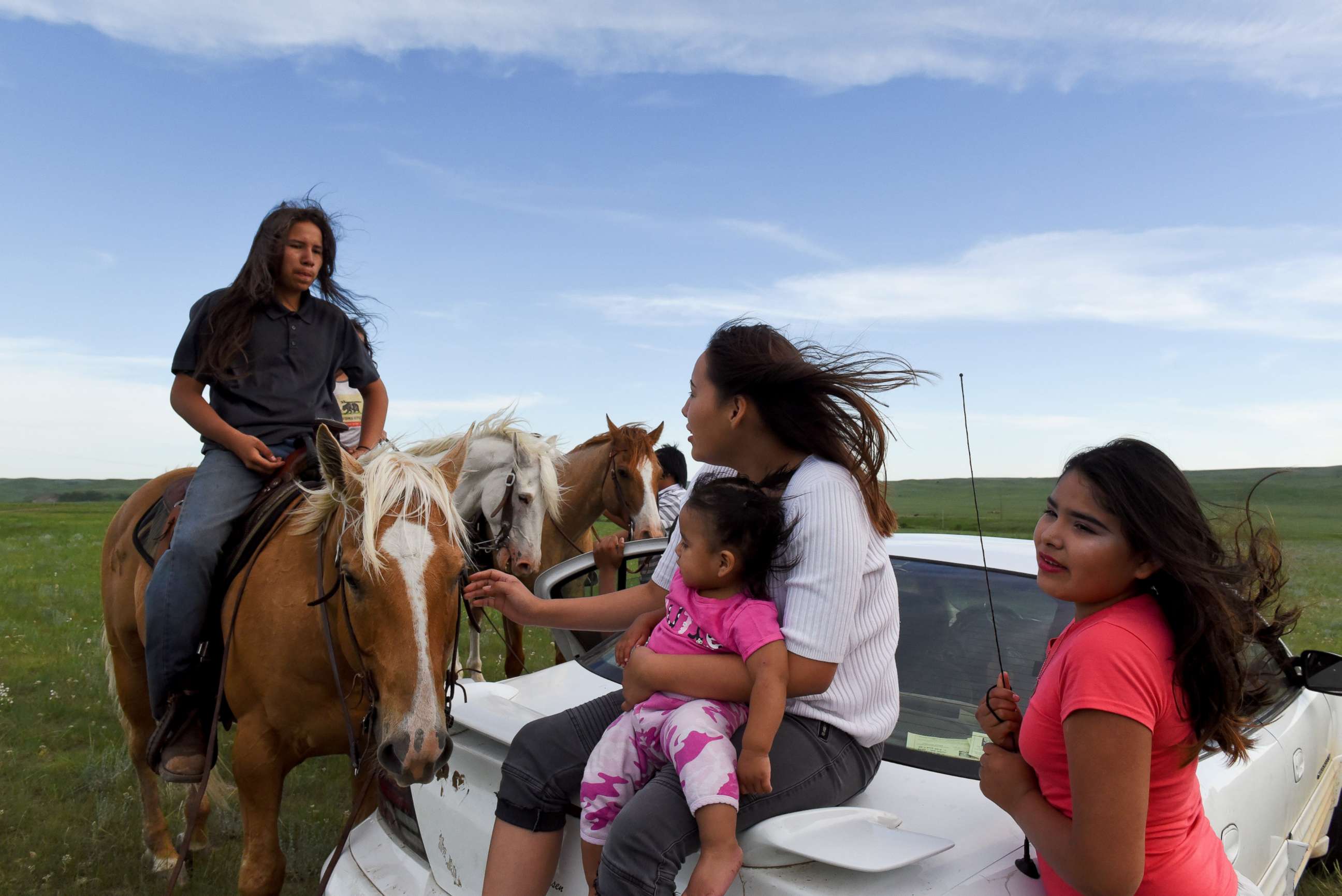 PHOTO: Angel Rose Lookinghorse, sitting with her younger cousins, Linda Lookinghorse and Maryann Lara, as she speaks to her brother, Jayden Lookinghorse, on horseback, at the Cheyenne River Reservation in Green Grass, South Dakota, May 31, 2018. 