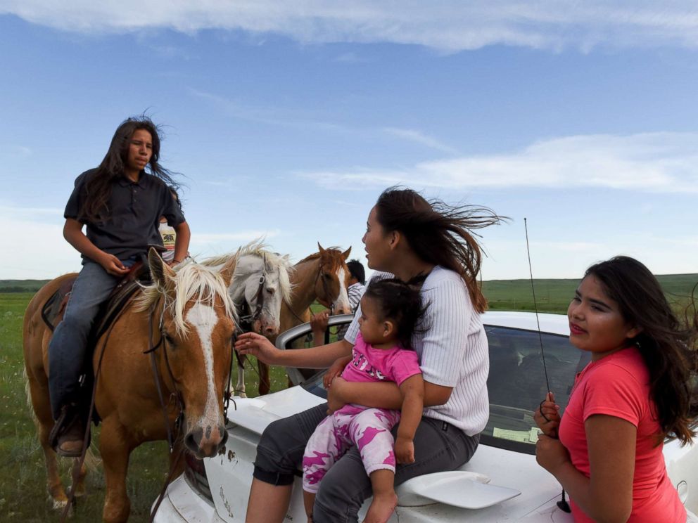 PHOTO: Angel Rose Lookinghorse, sitting with her younger cousins, Linda Lookinghorse and Maryann Lara, as she speaks to her brother, Jayden Lookinghorse, on horseback, at the Cheyenne River Reservation in Green Grass, South Dakota, May 31, 2018.