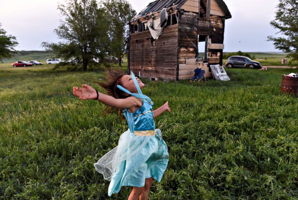 PHOTO: One of Beatrice Lookinghorse's granddaughters, Rozelynn Whitebull, plays near an abandoned house in the backyard of Beatrice Lookinghorse's trailer on the Cheyenne River Reservation in Green Grass, South Dakota, May 31, 2018. 