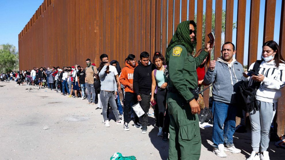 PHOTO: A U.S. Border Patrol agent checks for identification of immigrants as they wait in line to be processed after crossing from Mexico in Yuma, Ariz., May 21, 2022.