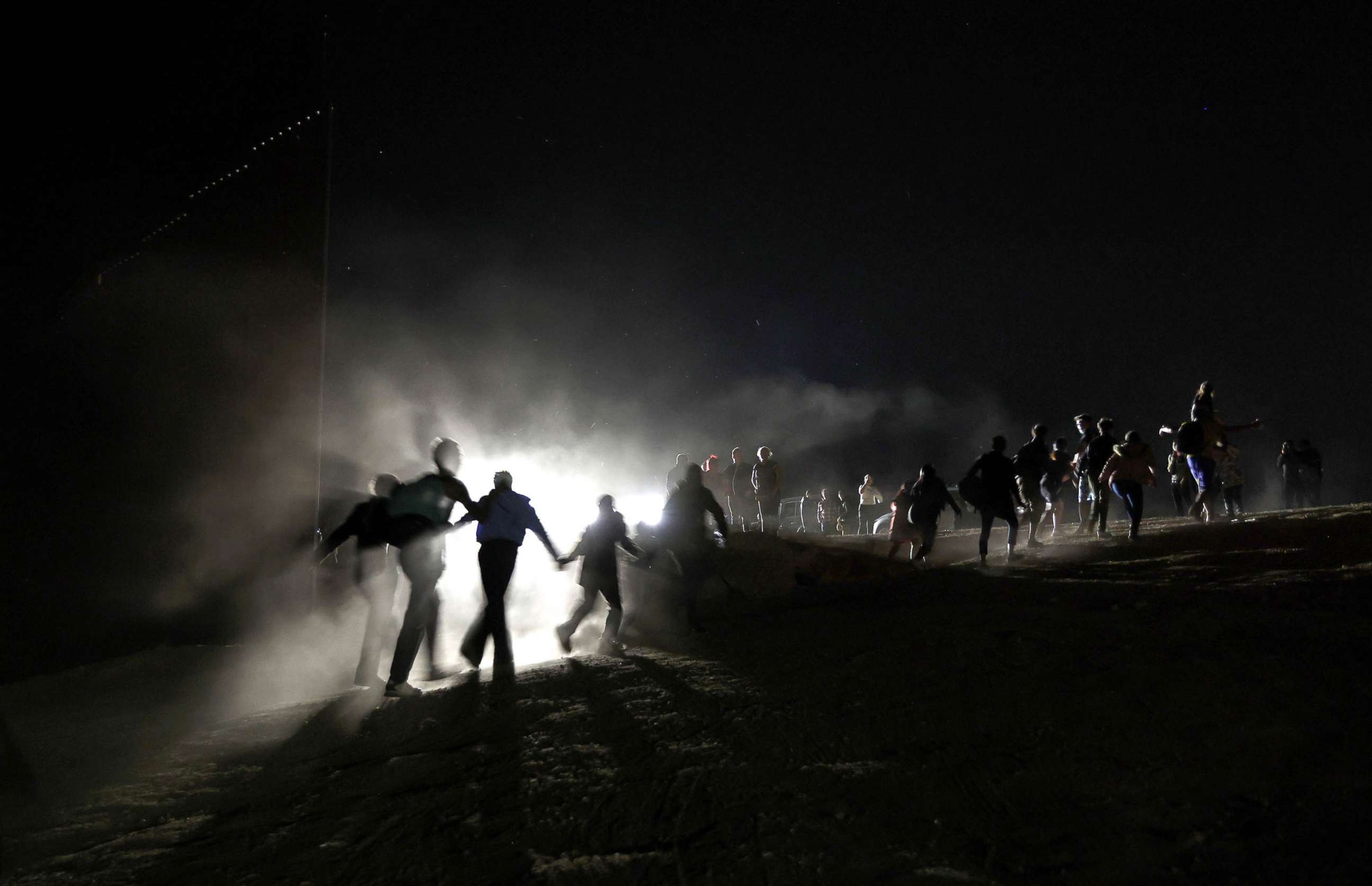 PHOTO: Immigrants cross through a gap in the U.S.-Mexico border barrier as others watch from above before being processed by the U.S. Border Patrol in Yuma, Ariz., May 23, 2022.