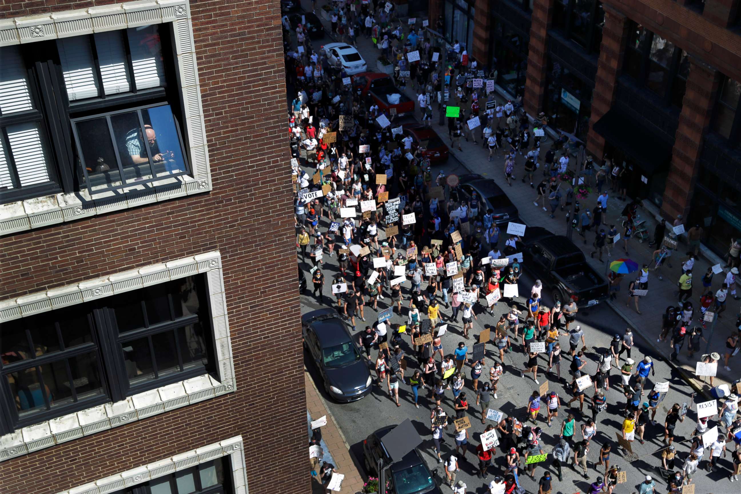 PHOTO: A person, upper left, holds a phone while watching from a window as protesters march in the street below Sunday, June 7, 2020, in St. Louis, Mo.