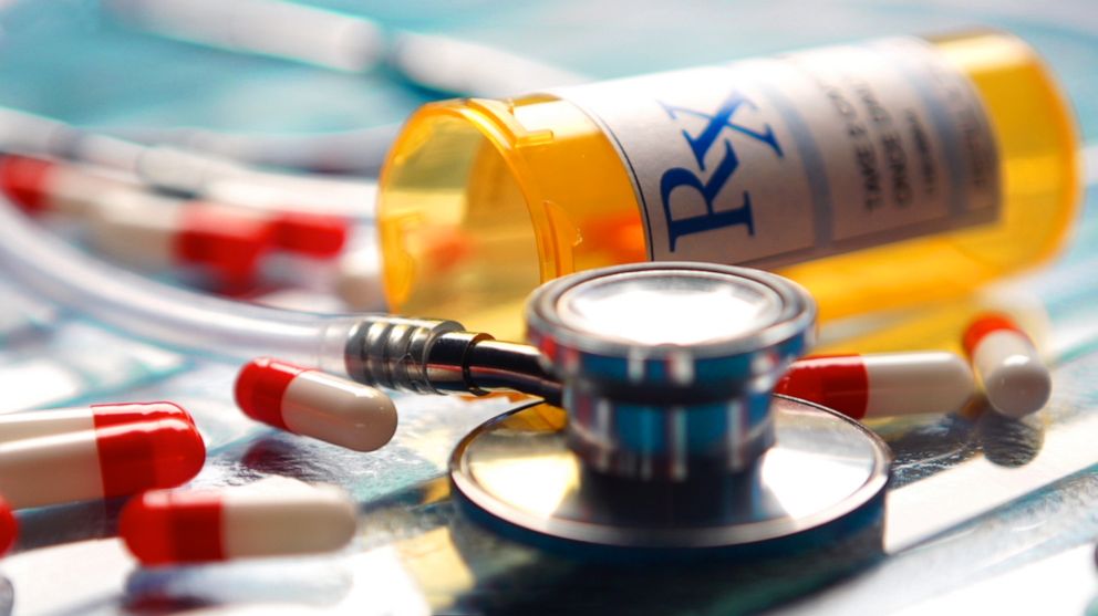 PHOTO: A stethoscope sits on a glass surface with an RX bottom and pills.