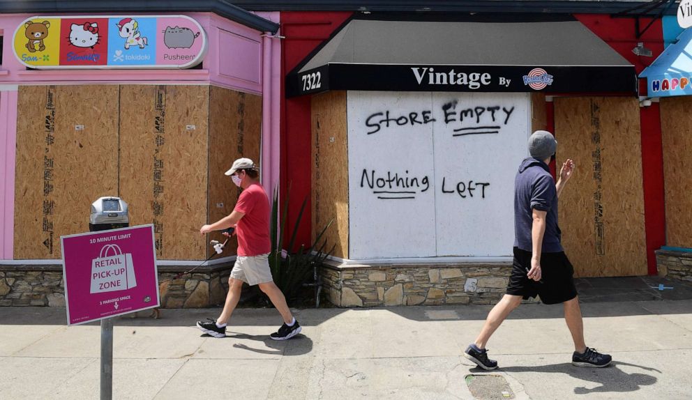 PHOTO: Pedestrians walk past boarded up storefronts on Melrose Avenue in Los Angeles, California on June 1, 2020, following a weekend of looting by people taking advantage of the protest situation in response to the death of George Floyd. 