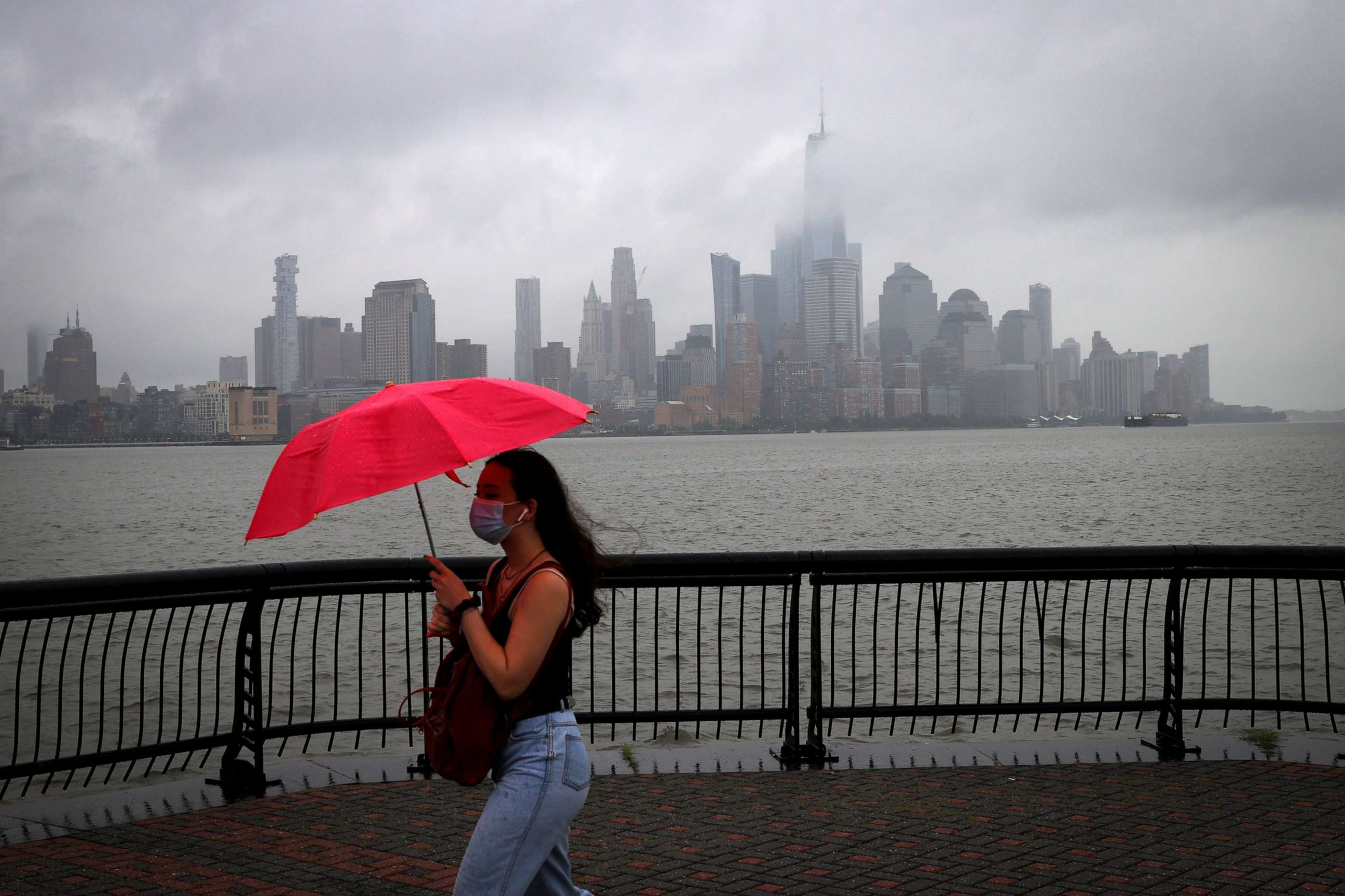 PHOTO: A woman, in Hoboken, N.J., shields herself from rain and wind with an umbrella as she walks along the Hudson River in front of the skyline of New York City, as Tropical Storm Fay is expected to sweep across the northeastern US, July 10, 2020.