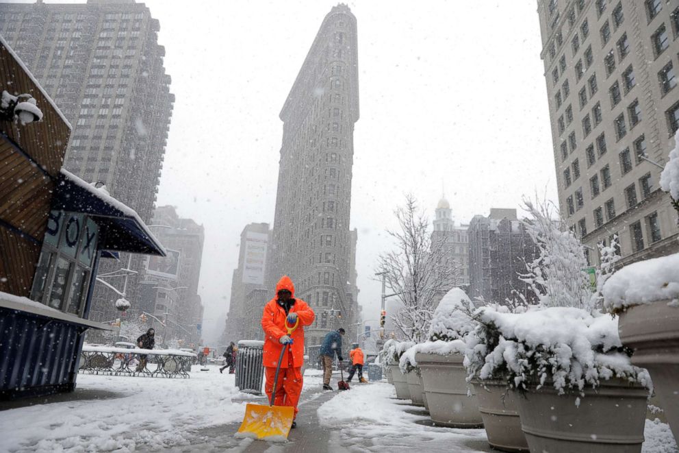 PHOTO: Workers clean snow off a sidewalk in front of the Flatiron building during a late season nor'easter in New York City, March 21, 2018.
