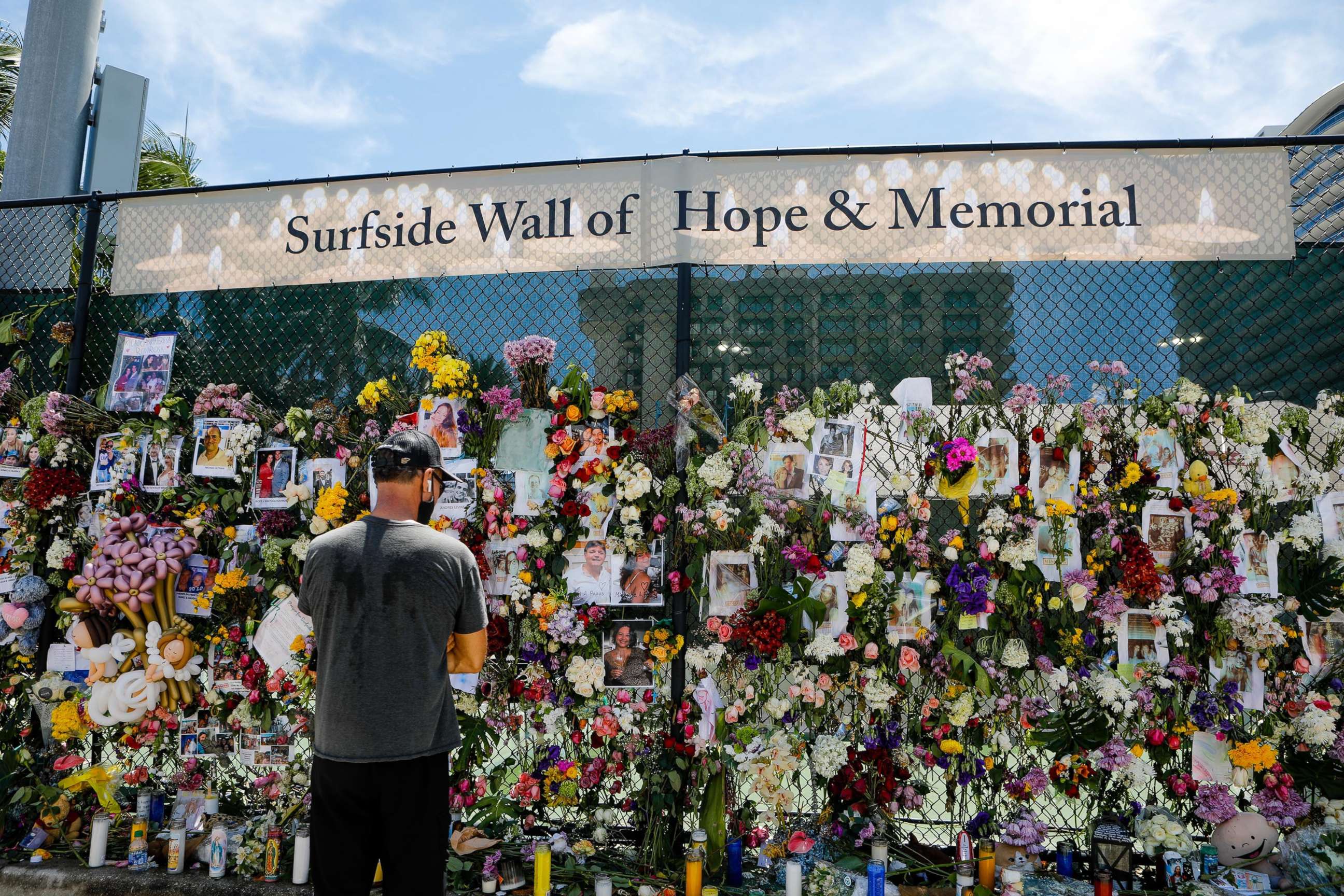 PHOTO: A man stands next to flowers and pictures of some of the missing from the partially collapsed 12-story Champlain Towers South condo building at the makeshift memorial for the victims of the building collapse in Surfside, Fla., July 02, 2021.