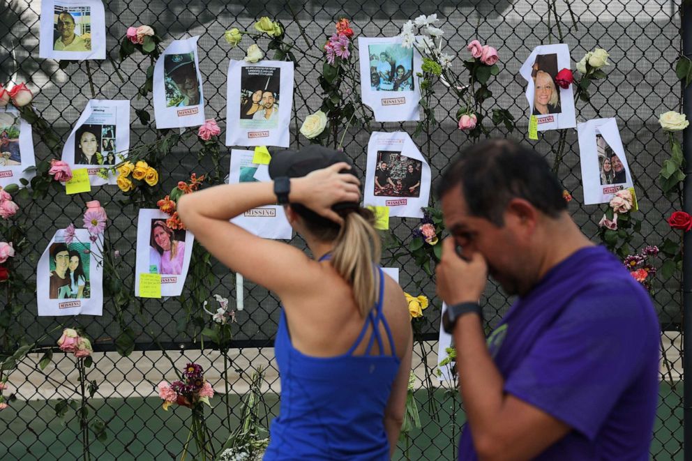 PHOTO: People look on at pictures of some of the missing from the partially collapsed 12-story Champlain Towers South condo building in Surfside, Fla., June 26, 2021.