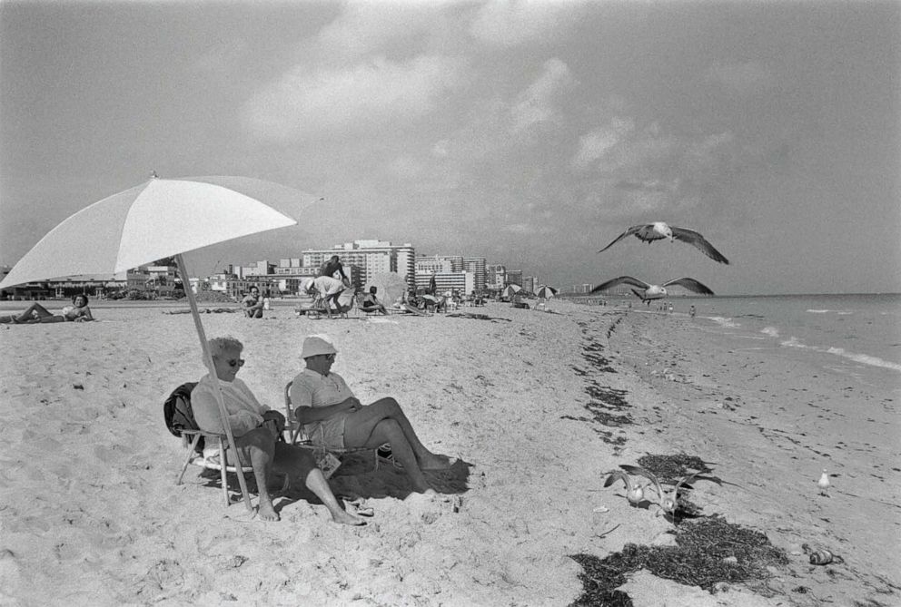 PHOTO: People sit under an umbrella on the 92nd Street Beach in Surfside, Fla., in December 1981.