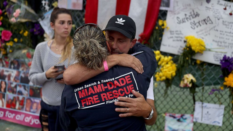 PHOTO: Search and Rescue personnel Maggie Castro hugs Pablo Langesfeld as they visit the memorial to the victims in the collapsed 12-story Champlain Towers South condo building, July 7, 2021, in Surfside, Fla.