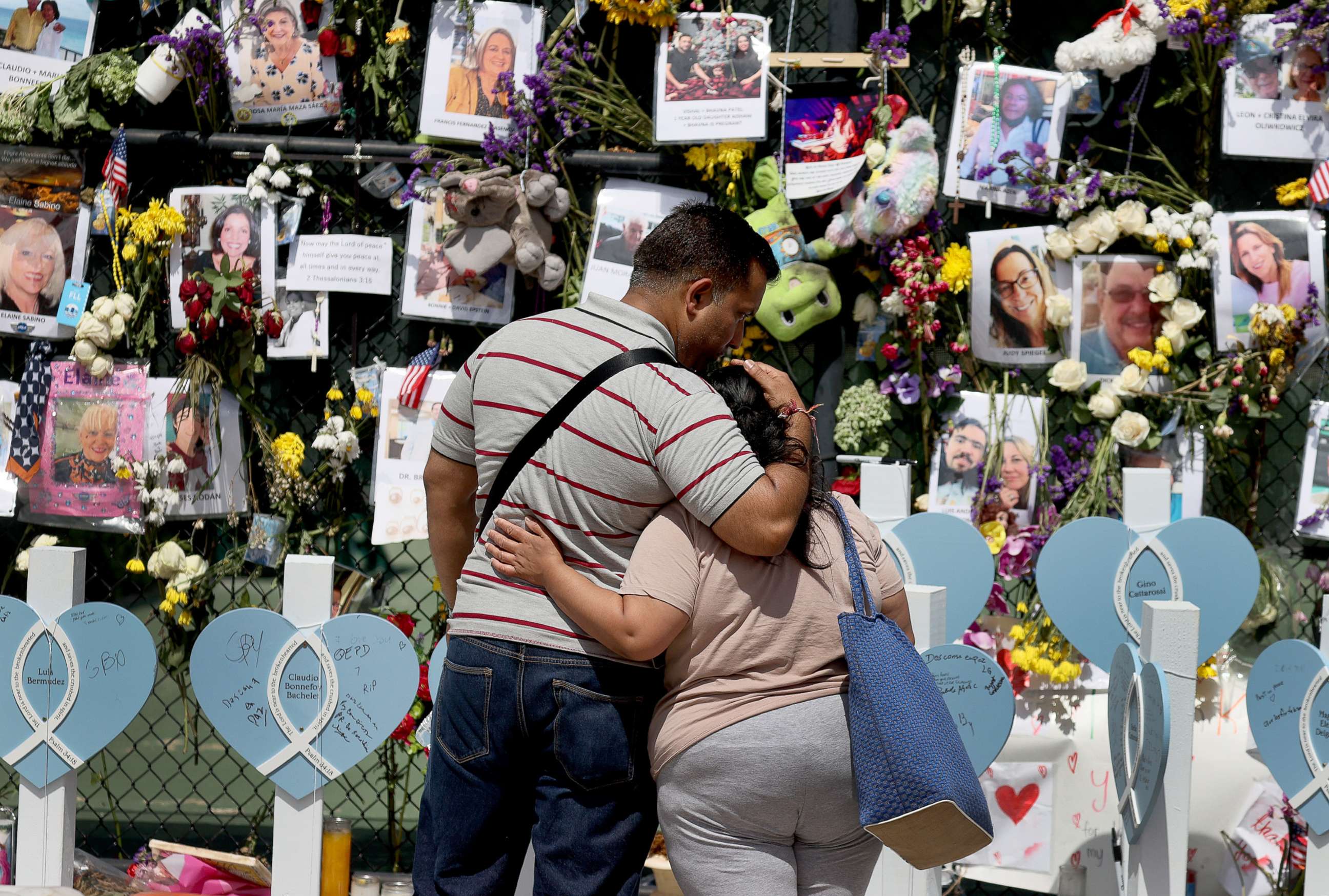PHOTO: People hug as they look at a memorial that has pictures of some of the victims of the collapsed 12-story Champlain Towers South condo building on July 08, 2021, in Surfside, Fla.