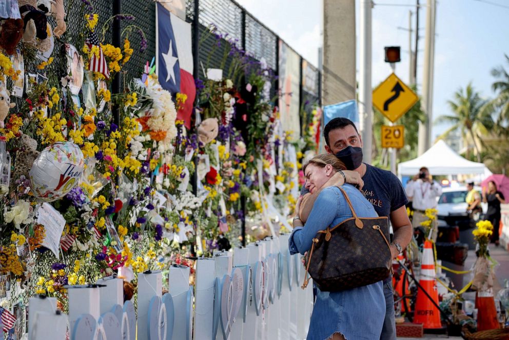 PHOTO: Laura Solla weeps as she and William Chamak place flowers near the memorial site for victims of the collapsed 12-story Champlain Towers South condo building on July 8, 2021, in Surfside, Fla.