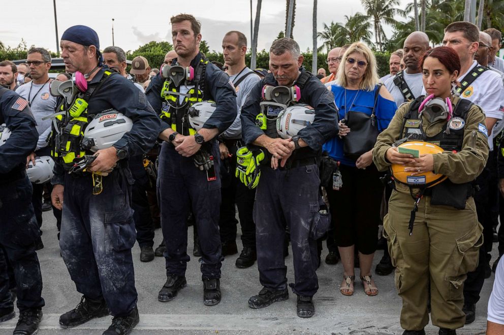 PHOTO: Members of a search and rescue team stand in front of the rubble that once was Champlain Towers South during a prayer ceremony in Surfside, Fla., Wednesday, July 7, 2021.