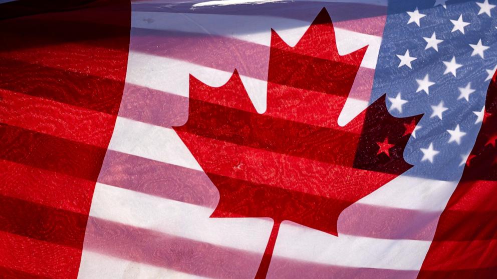 PHOTO: Sunlight shines through the flags of Canada and the United States, held together by a protester outside on Parliament Hill in Ottawa, Feb. 1, 2025.