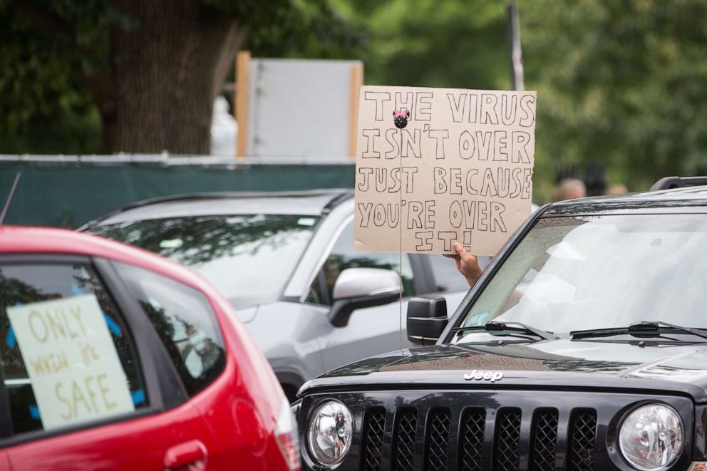 PHOTO: A person in a vehicle holds a sign that reads "The Virus Isn't Over Just Because You're Over It!" during a standout protest organized by the American Federation of Teachers at the Massachusetts State House in Boston on Aug. 19, 2020.