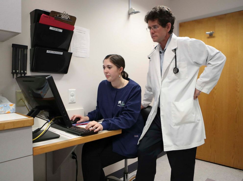 PHOTO: Dr. James Gill speaks with a patient via teleheath video app as medical scribe Karli Taneyhill records notes during a virtual visit at the Family Medicine at Greenhill practice in Wilmington, Del., April 1, 2020.
