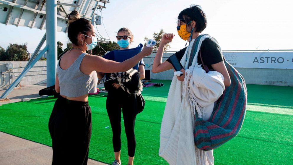 PHOTO: A hostess from Astro Gong Yoga Studio checks a woman's temperature before she attends a yoga class being held on a roof top parking lot, as the studio cannot be open to the public amid the coronavirus pandemic, in Los Angeles on August 4, 2020.