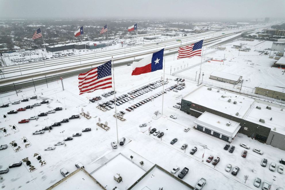 PHOTO: In an aerial view, U.S. and Texas state flags fly over car dealerships as light traffic moves through snow and ice, Feb. 3, 2022, in Irving, Texas. 