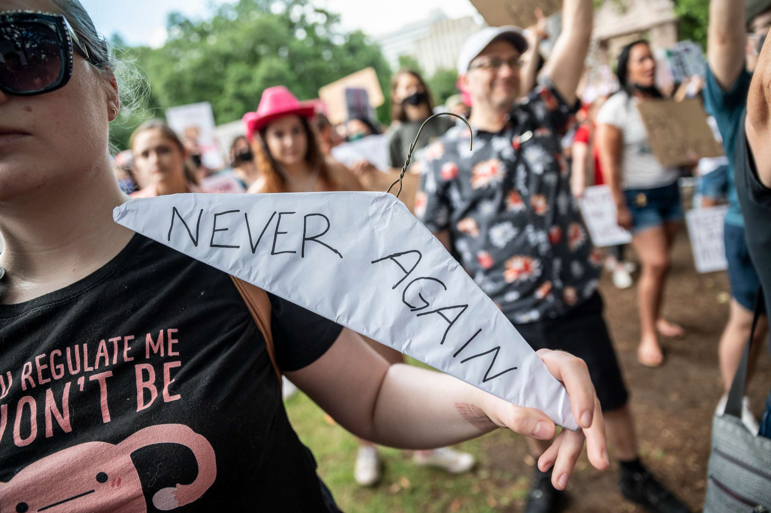 PHOTO: A woman holds a clothes hanger wrapped in paper with "Never again" written on it at a protest for abortion rights outside the Texas state capitol on May 29, 2021, in Austin.