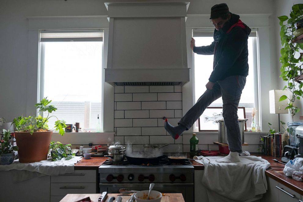 PHOTO: Jorge Sanhueza-Lyon stands on his kitchen counter to warm his feet over his gas stove, Feb. 16, 2021, in Austin, Texas.