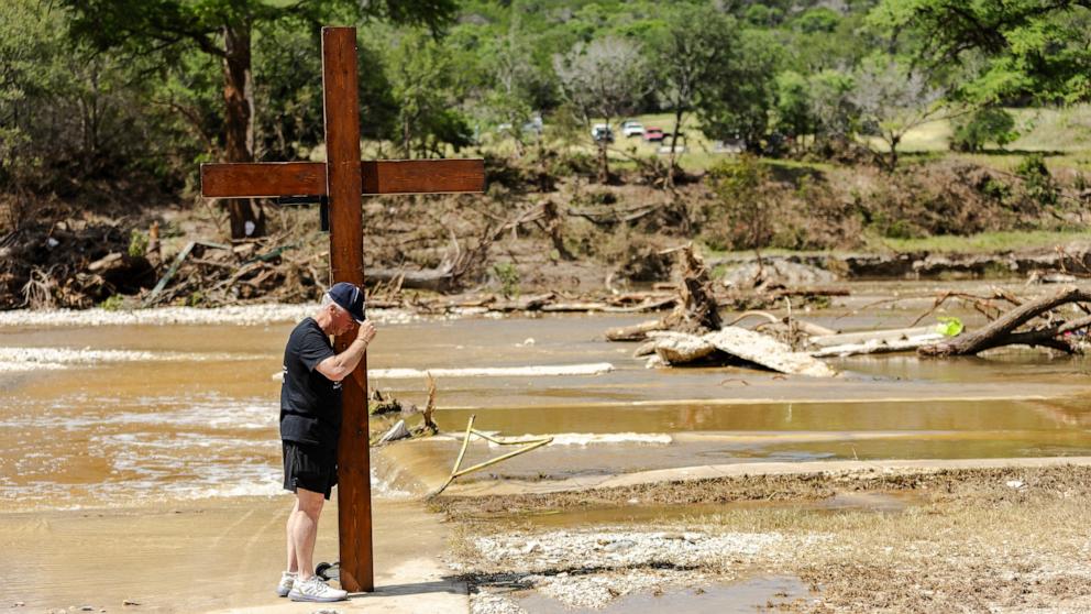 PHOTO: Dan Beazley prays at the bank of the Guadalupe River while holding a large wooden cross, July 8, 2025 in Ingram, Texas. 