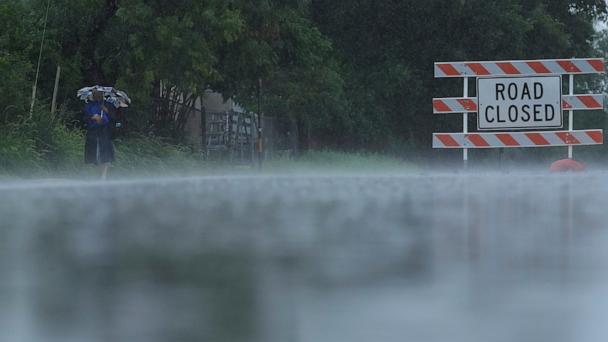 A woman walks in the rain past a closed street near the Guadalupe River, Sunday, July 13, 2025, in Kerrville, Texas.