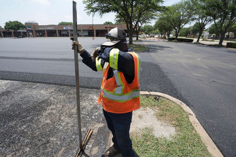 PHOTO: Miguel takes a break from shoveling asphalt during a parking lot restoration job in Richardson, Texas on June 20, 2023.