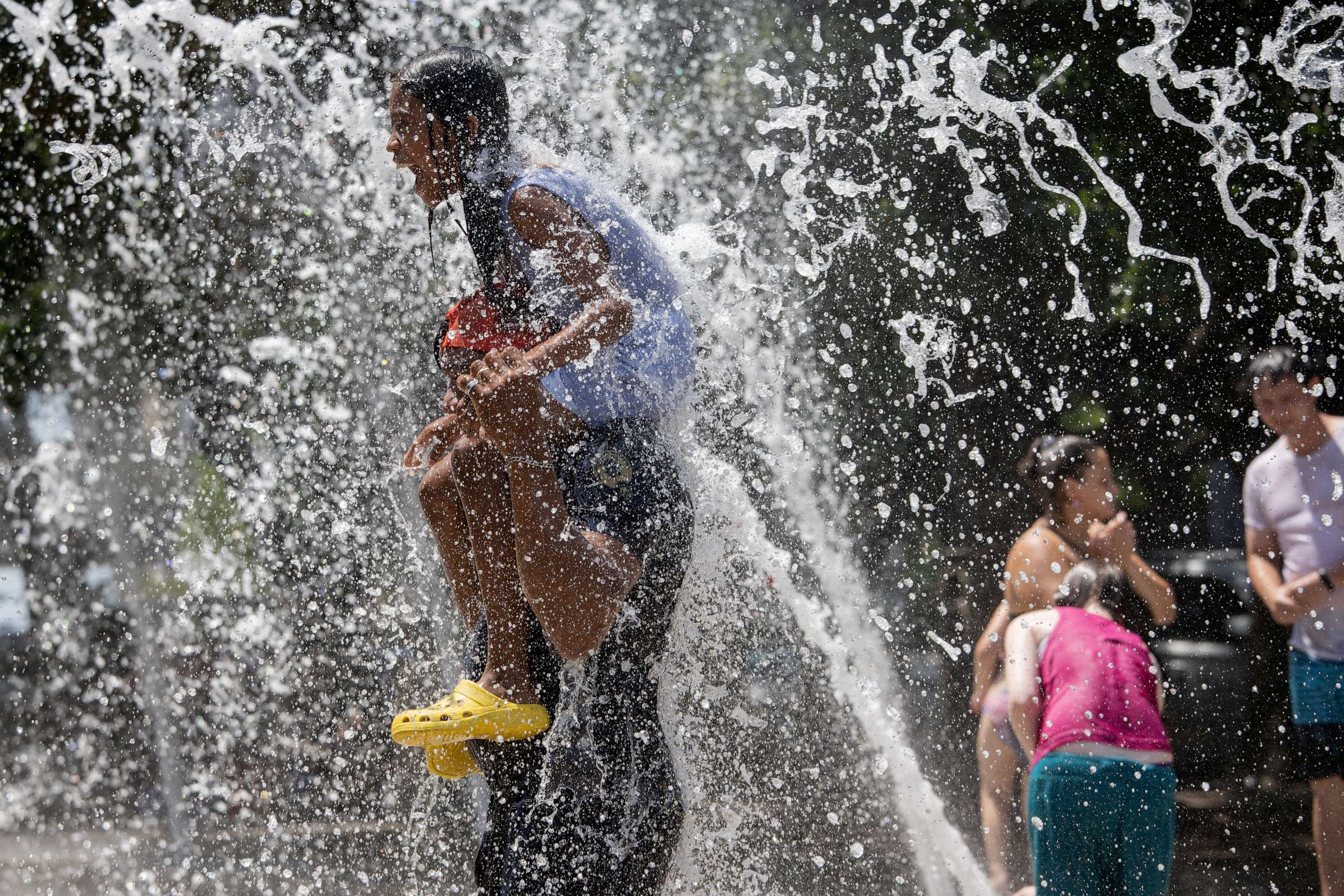PHOTO: Fernando Aguilar, from El Salvador, carries his 8-year-old daughter Dannesy through the jet streams of Gateway Fountains at Discovery Green to escape the hot weather on Father's Day in Houston, June 18, 2023.