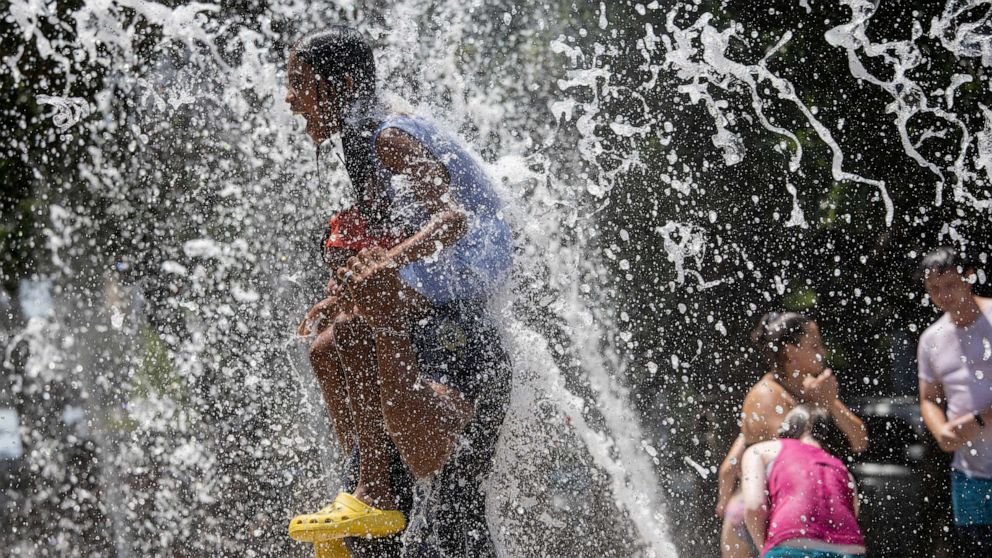 PHOTO: Fernando Aguilar, from El Salvador, carries his 8-year-old daughter Dannesy through the jet streams of Gateway Fountains at Discovery Green to escape the hot weather on Father's Day in Houston, June 18, 2023.