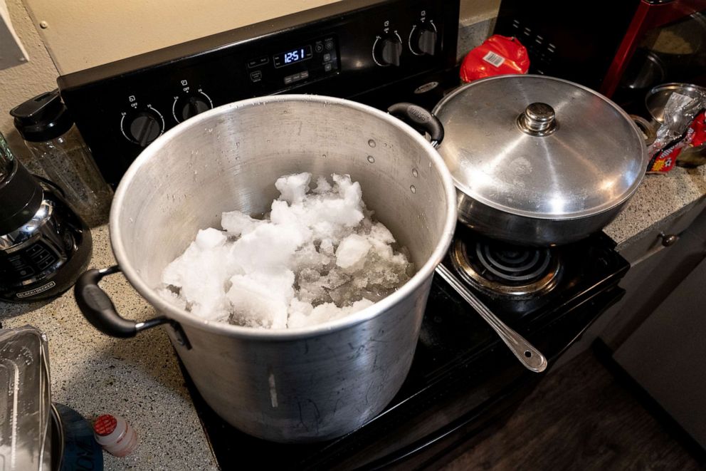 PHOTO: A family whose electricity was recently restored, but who still has no water, melts snow on their stovetop to have water to flush toilets and wash dishes in Austin, Texas on Feb. 17, 2021.