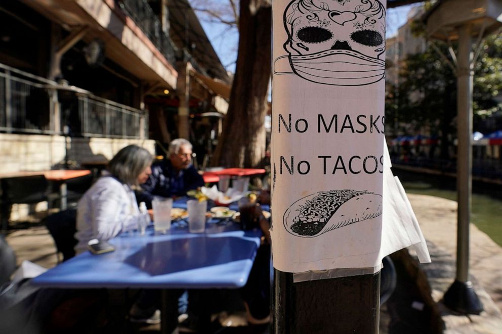 PHOTO: A sign requiring masks is seen near diners eating at a restaurant on the River Walk, March 3, 2021, in San Antonio.
