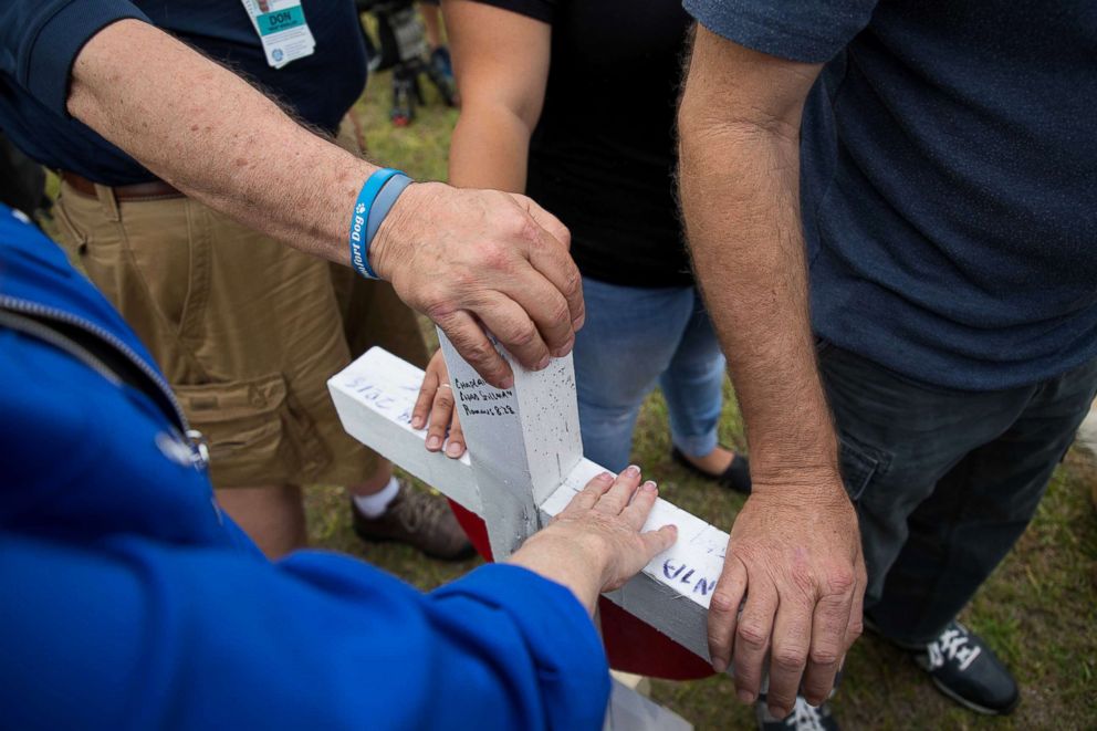 PHOTO:  Hands are placed on a cross at the makeshift memorial outside Santa Fe High School during a moment of silence at 10am, May 21, 2018, in Santa Fe, Texas.