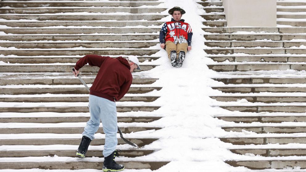 PHOTO: Jimmy Pavelich sleds down the steps of the Mary Couts Burnett Library as Michael Manson shovels snow at Texas Christian University after a snow storm on Feb. 17, 2021, in Fort Worth, Texas.