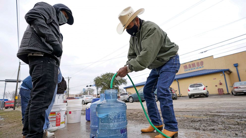 PHOTO: Leovardo Perez, right, fills a water jug using a hose from a public park water spigot, Feb. 18, 2021, in Houston.