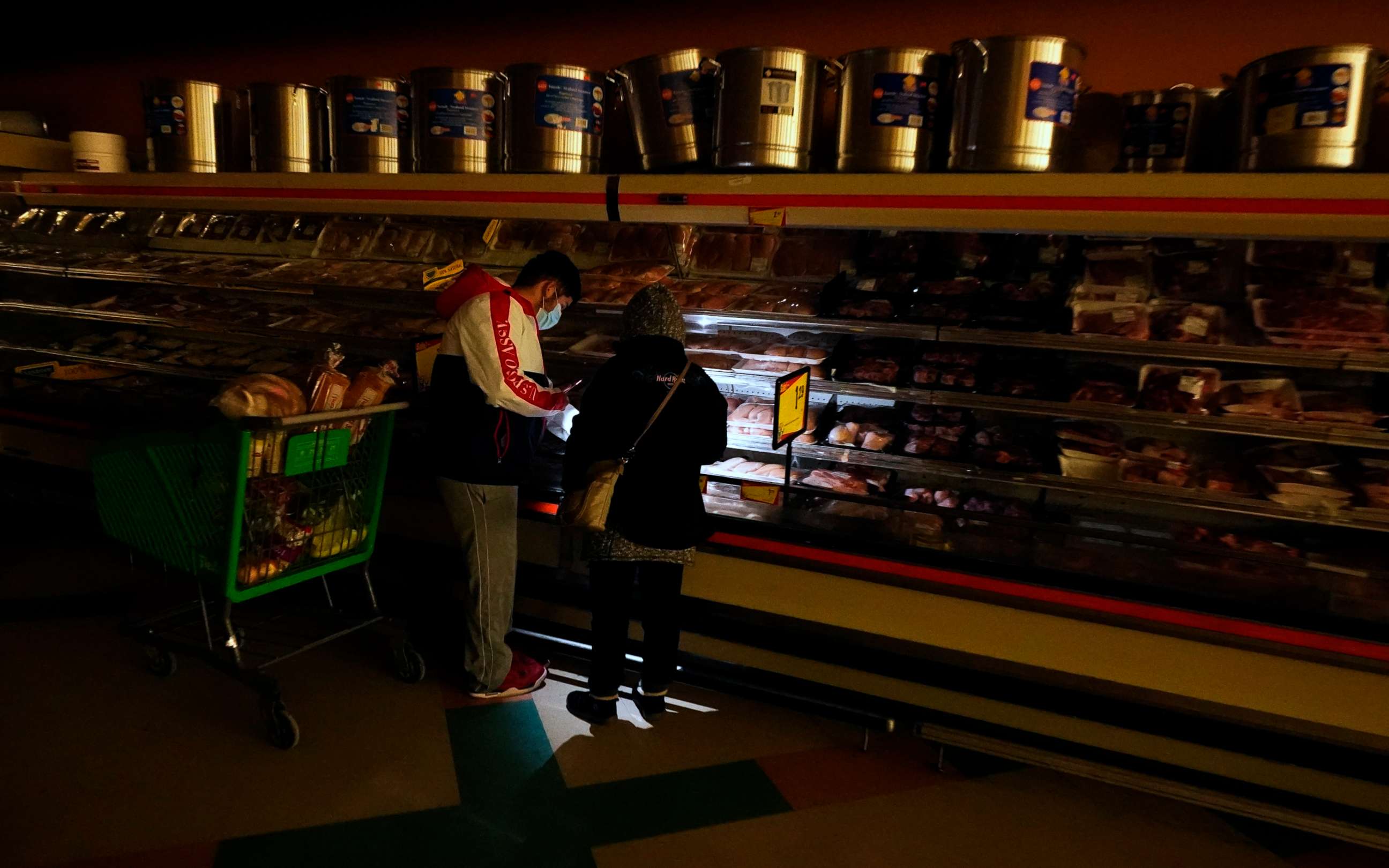 PHOTO: Customers use the light from a cell phone to look in the meat section of a grocery store Tuesday, Feb. 16, 2021, in Dallas.