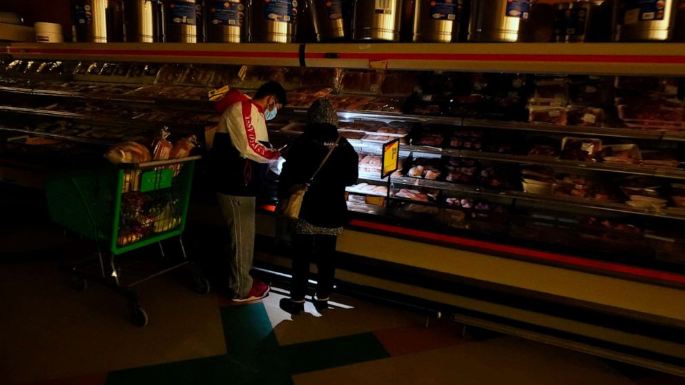 PHOTO: Customers use the light from a cell phone to look in the meat section of a grocery store Tuesday, Feb. 16, 2021, in Dallas.