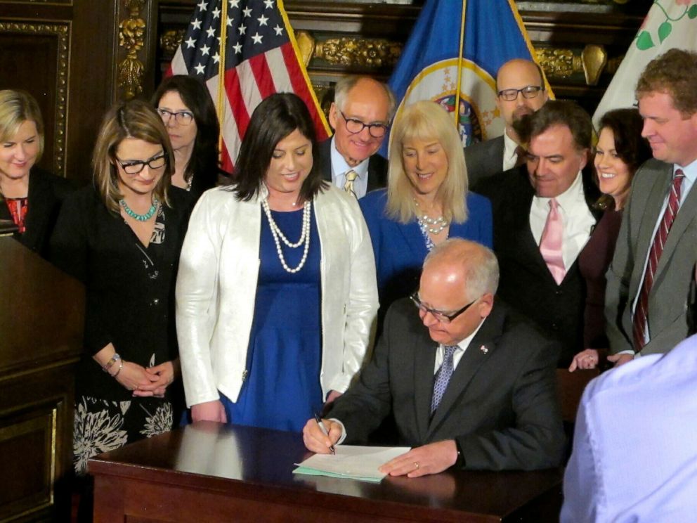 PHOTO: Jenny Teeson, center in white, of Andover, Minn., looks on as Minnesota Gov. Tim Walz signs a bill at the Capitol in St. Paul, on Thursday, May 2, 2019.