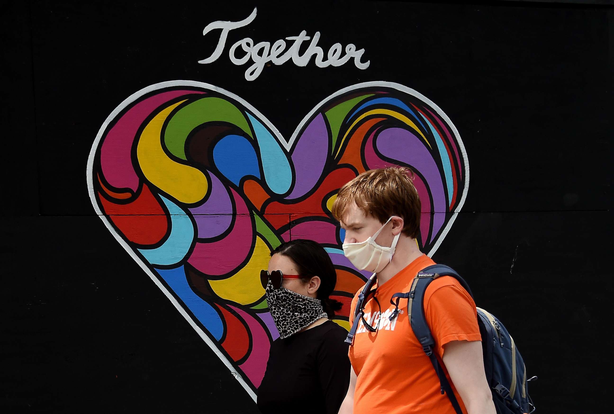 PHOTO: People wearing face masks walk past a mural of encouragement displayed outside a store amid the coronavirus pandemic in Washington, D.C., on May 19, 2020.