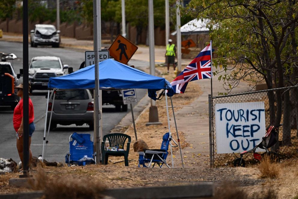 PHOTO: The Flag of Hawaii waves by a sign reading "Tourist Keep Out" in the aftermath of the Maui wildfires in Lahaina, Hawaii, on August 16, 2023.