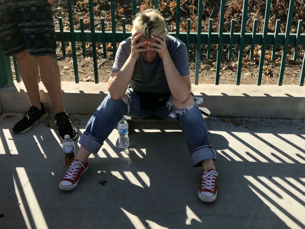 An unidentified woman sits next to witnesses on a sidewalk after a gunman barricaded himself inside a Trader Joe's in Los Angeles, July 21, 2018.