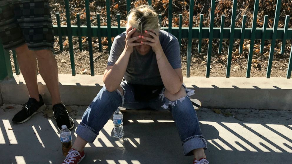 An unidentified woman sits next to witnesses on a sidewalk after a gunman barricaded himself inside a Trader Joe's in Los Angeles Saturday, July 21, 2018. Police believe a man involved in a standoff at the supermarket shot his grandmother and girlfriend.