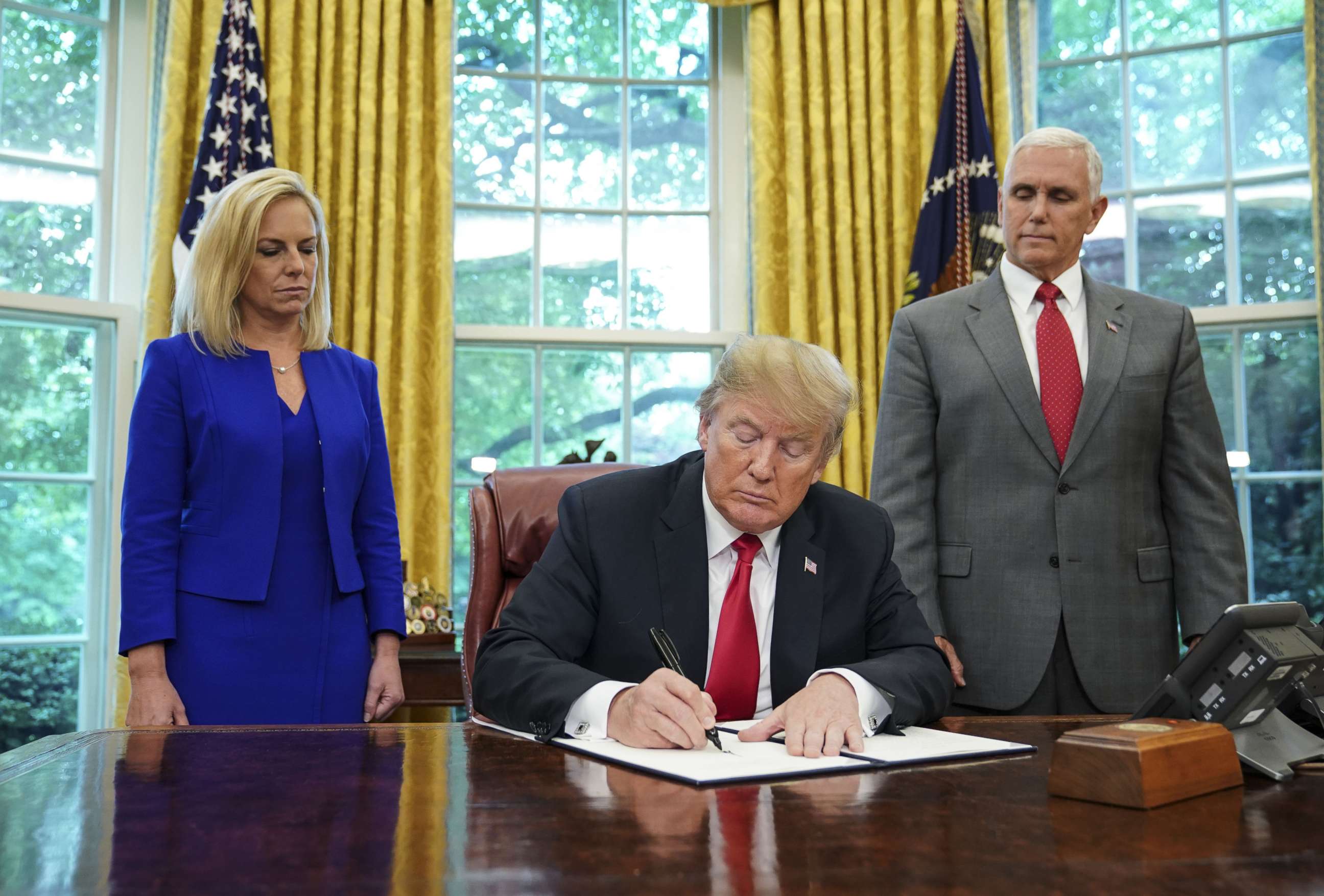 PHOTO: Homeland Security Secretary Kirstjen Nielsen (L) and Vice President Mike Pence watch as President Donald Trump signs an executive order on immigration in the Oval Office of the White House, June 20, 2018.