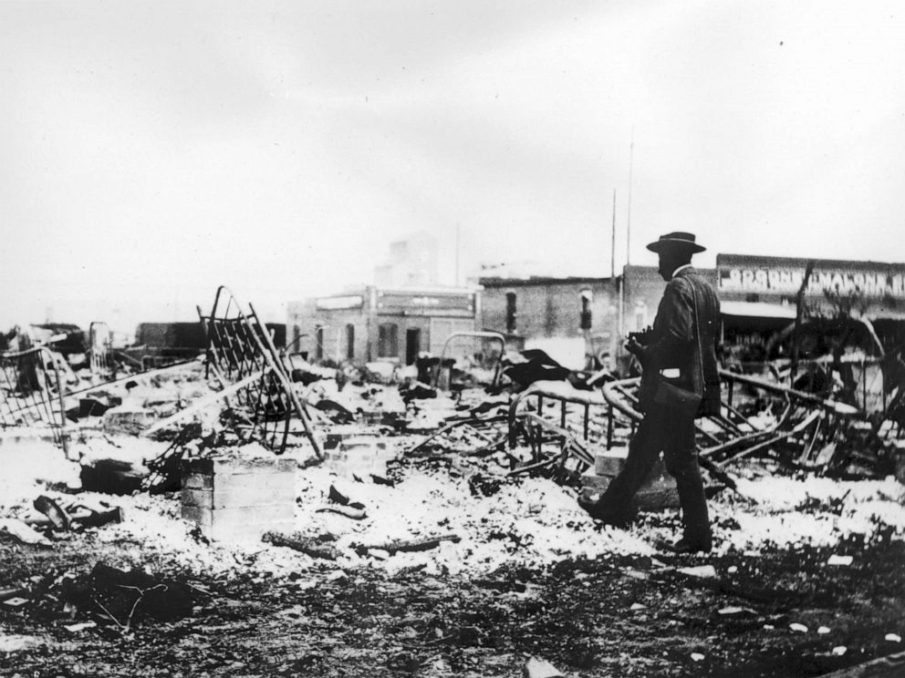 PHOTO: A man with a camera looks at the skeletons of iron beds above the ashes of a burned-out block after the Tulsa Race Riot, Tulsa, Oklahoma, 1921.